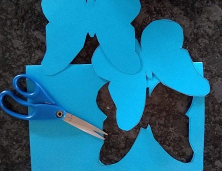 Cutting butterfly shapes out of blue paper with scissors