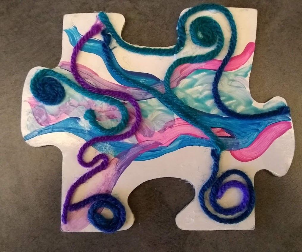 puzzle piece decorated with acrylic paint and yarn