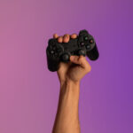Unrecognizable young man holding video game joystick in neon light, closeup of hand